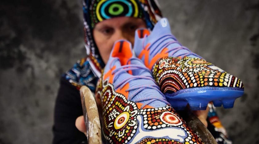 Indigenous artist Daren Dunn holds up the boots he painted for Jack Wighton